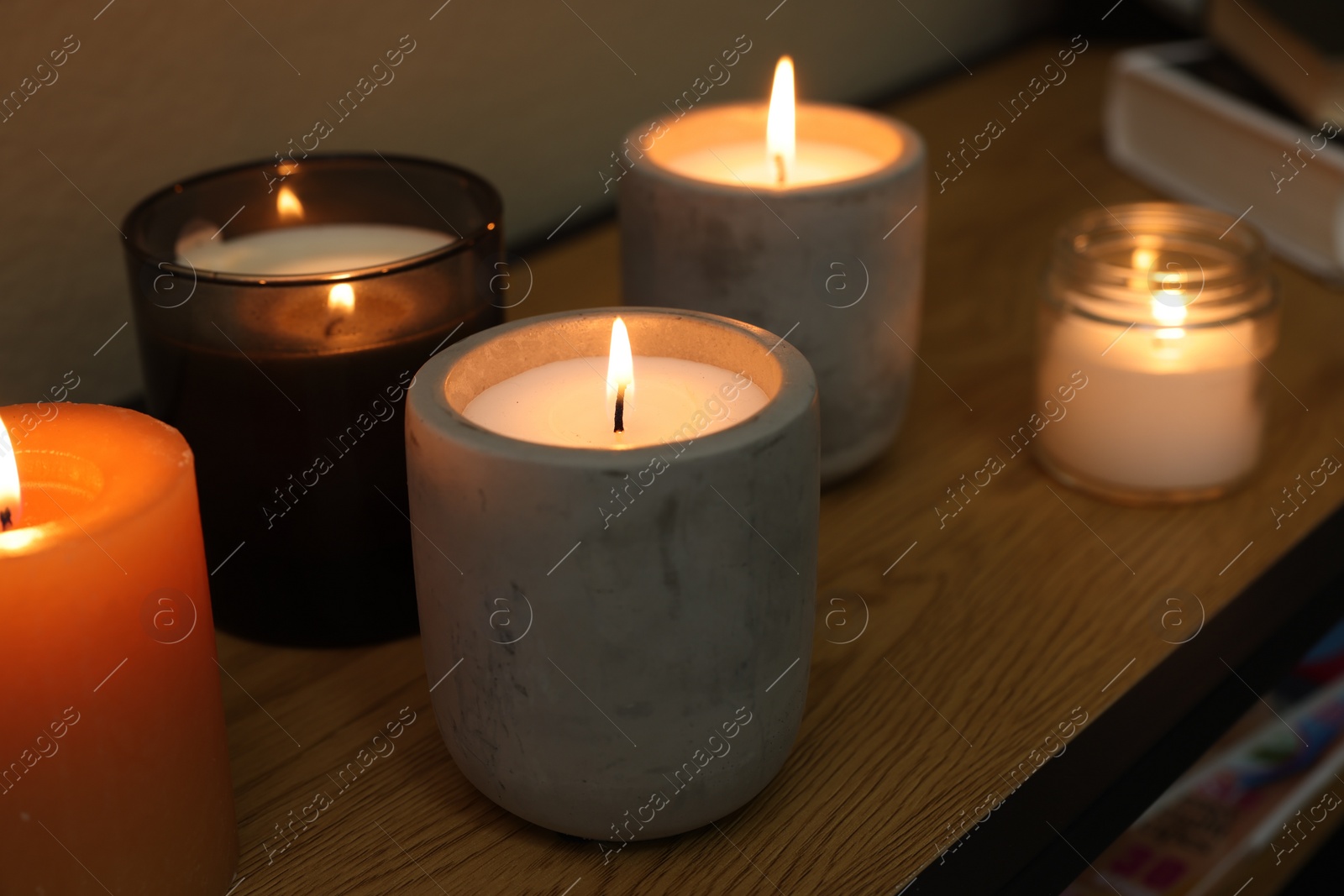 Photo of Lit candles in different holders on wooden table indoors