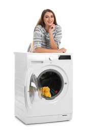 Young woman standing near washing machine with dirty laundry on white background