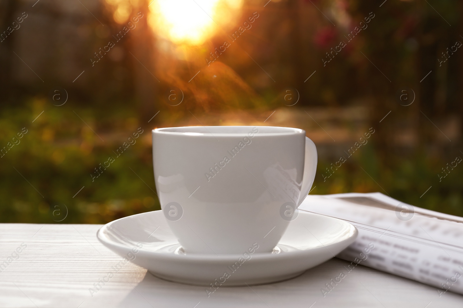 Photo of White cup with coffee and newspaper on wooden table in morning outdoors