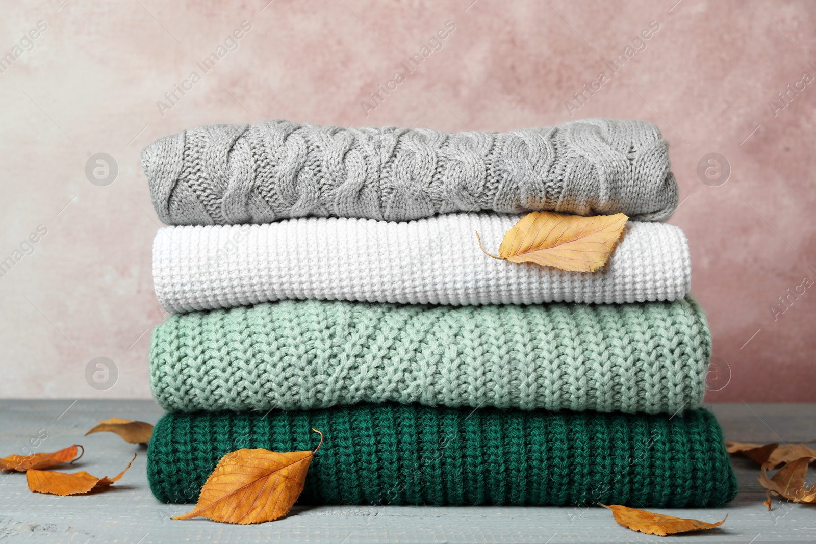 Photo of Stack of warm clothes and autumn leaves on grey wooden table against light background