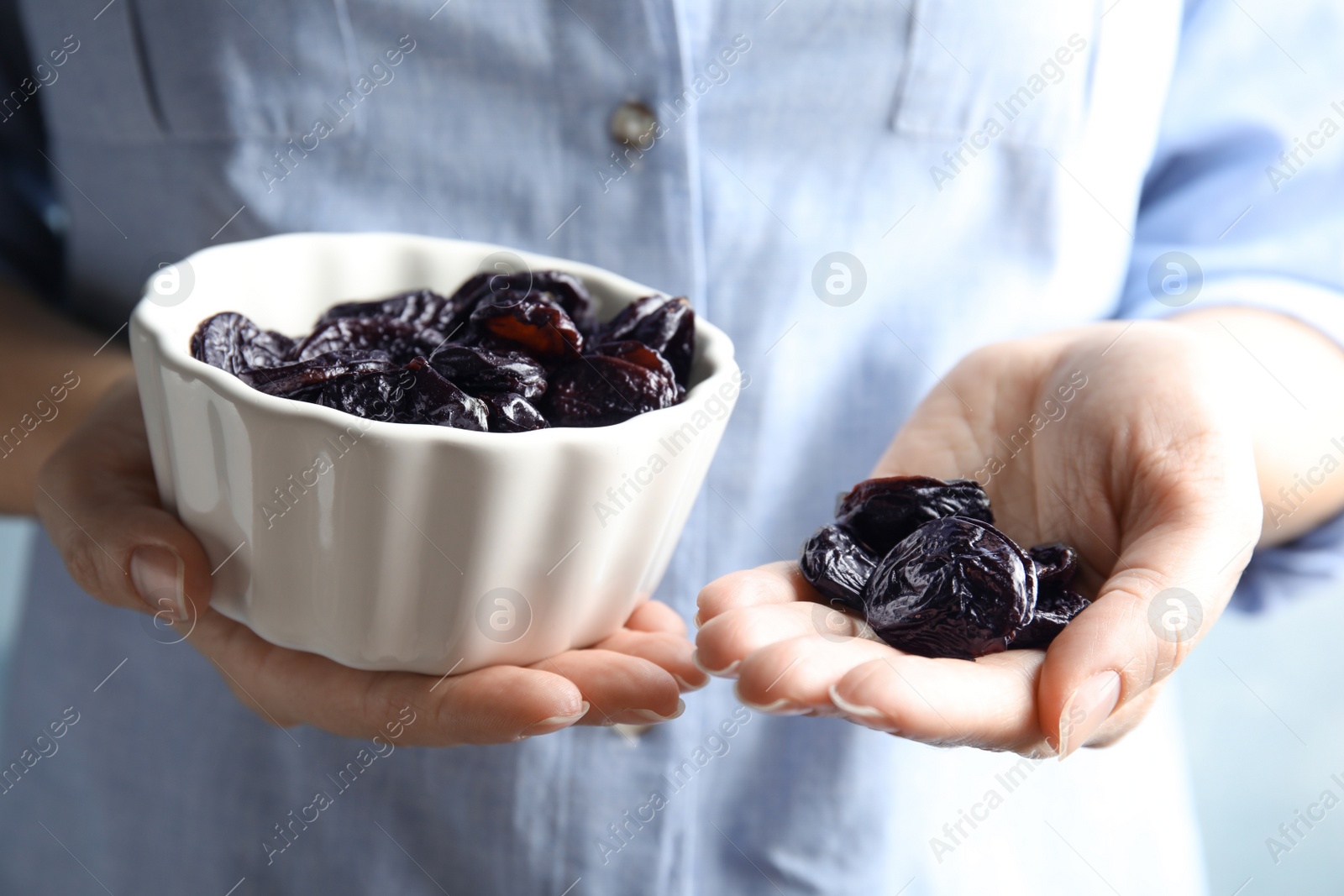 Photo of Woman holding bowl and handful of dried plums, closeup. Healthy fruit