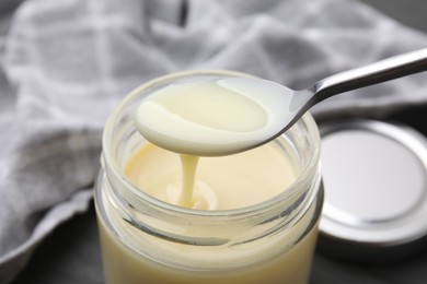 Photo of Condensed milk flowing down from spoon into jar on table, closeup