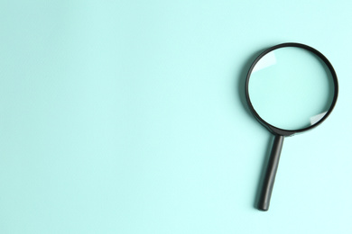 Top view of magnifying glass on light blue background, space for text. Search concept