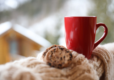 Photo of Fresh coffee, tasty cookies and knitted fabric outdoors on winter morning. Space for text