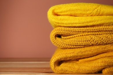Photo of Stack of folded knitted sweaters on wooden table, closeup. Space for text