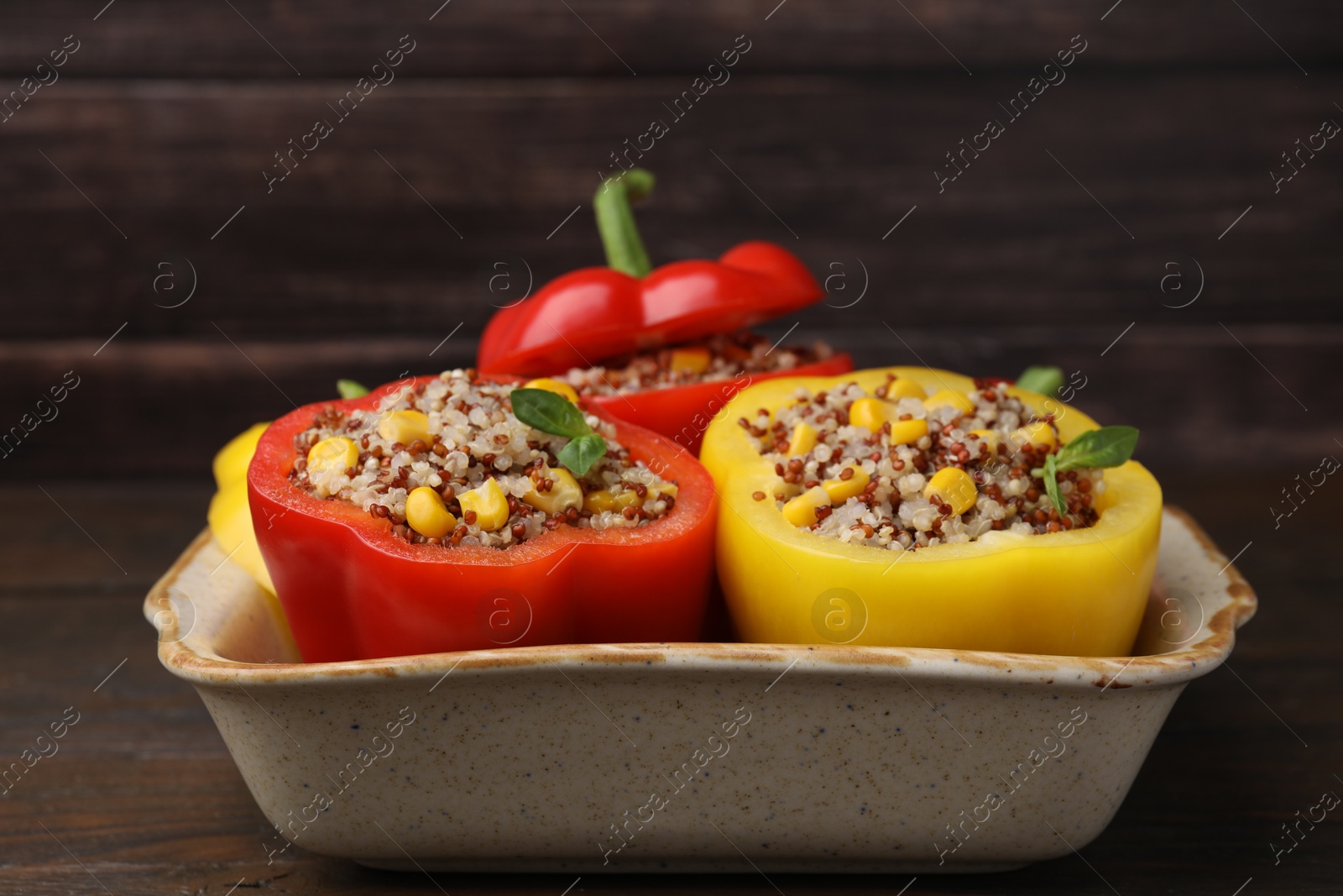 Photo of Quinoa stuffed bell peppers and basil in baking dish on wooden table, closeup