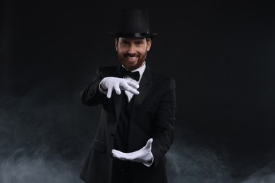 Happy magician holding something in smoke on black background