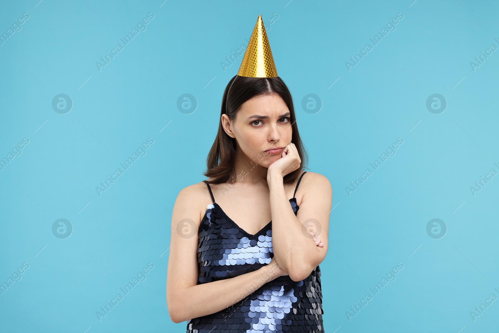 Photo of Sad young woman in party hat on light blue background