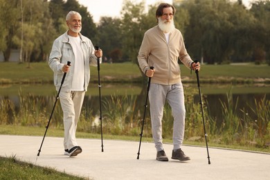 Photo of Two senior friends performing Nordic walking outdoors
