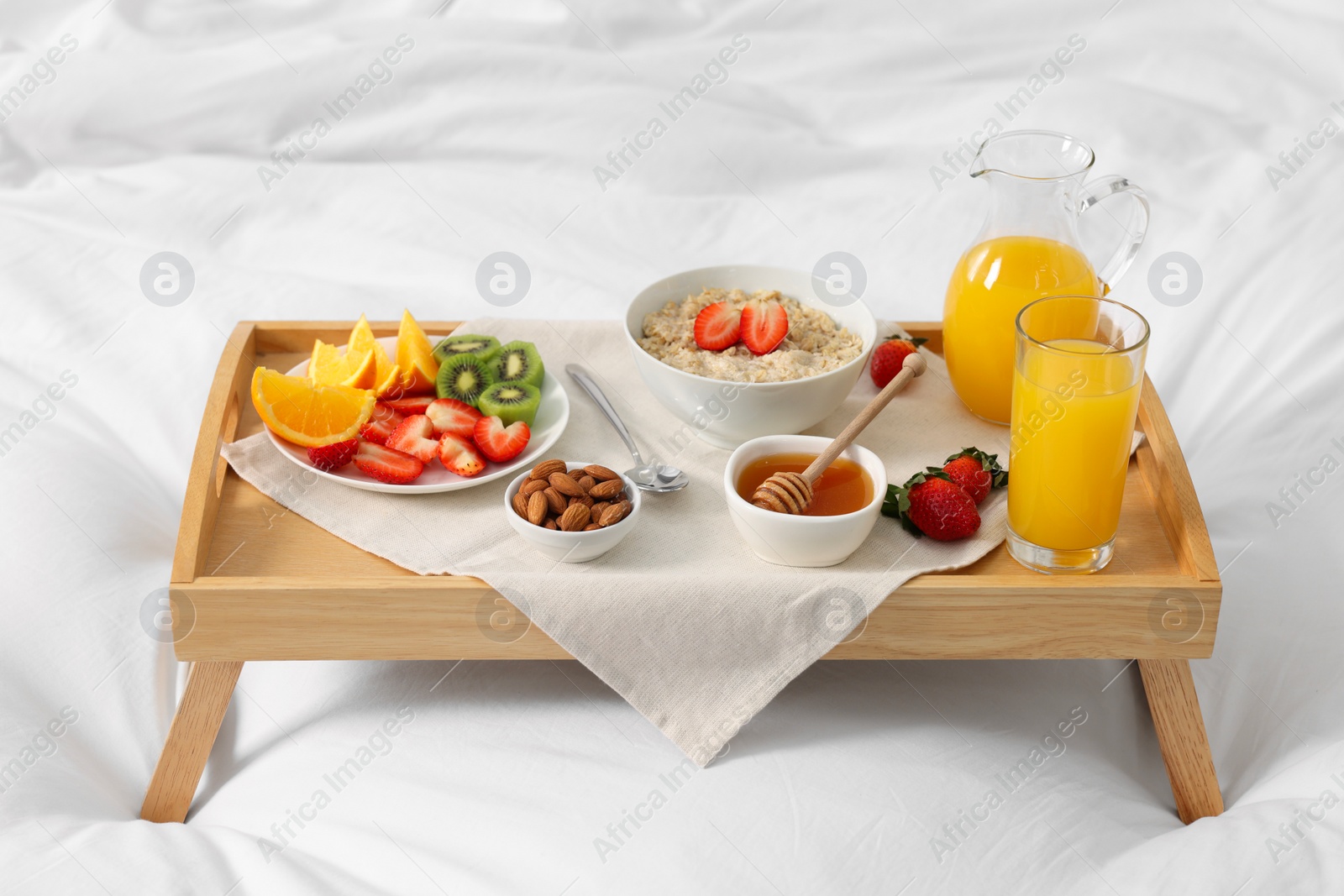 Tasty breakfast served in bed. Oatmeal, juice, fruits, almonds and honey on wooden tray Photo of Tasty breakfast served in bed. Oatmeal, juice, fruits, almonds and honey on wooden tray
