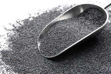 Poppy seeds and metal scoop on white table, closeup