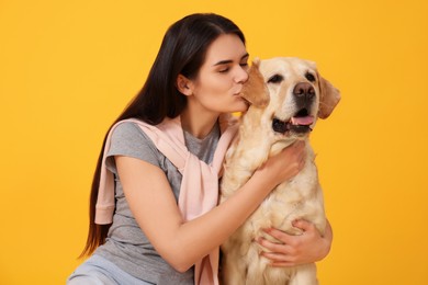 Happy woman kissing cute Labrador Retriever on orange background