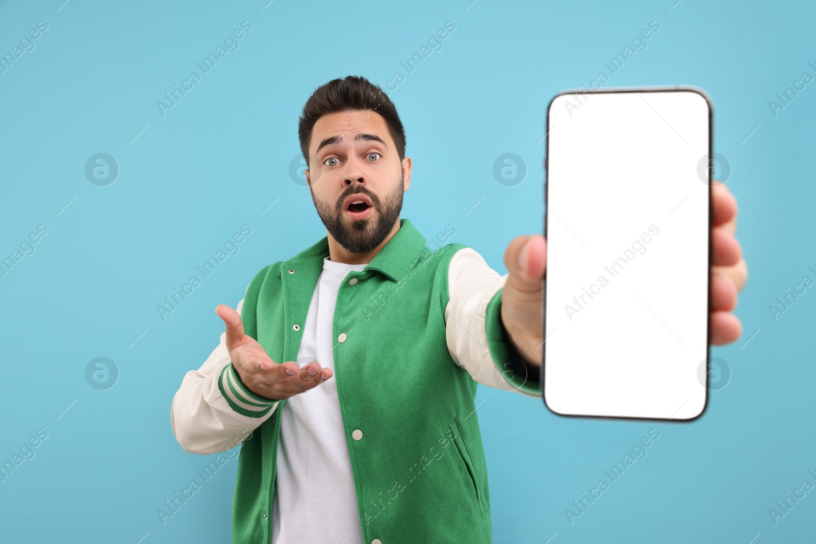 Photo of Surprised man showing smartphone in hand on light blue background