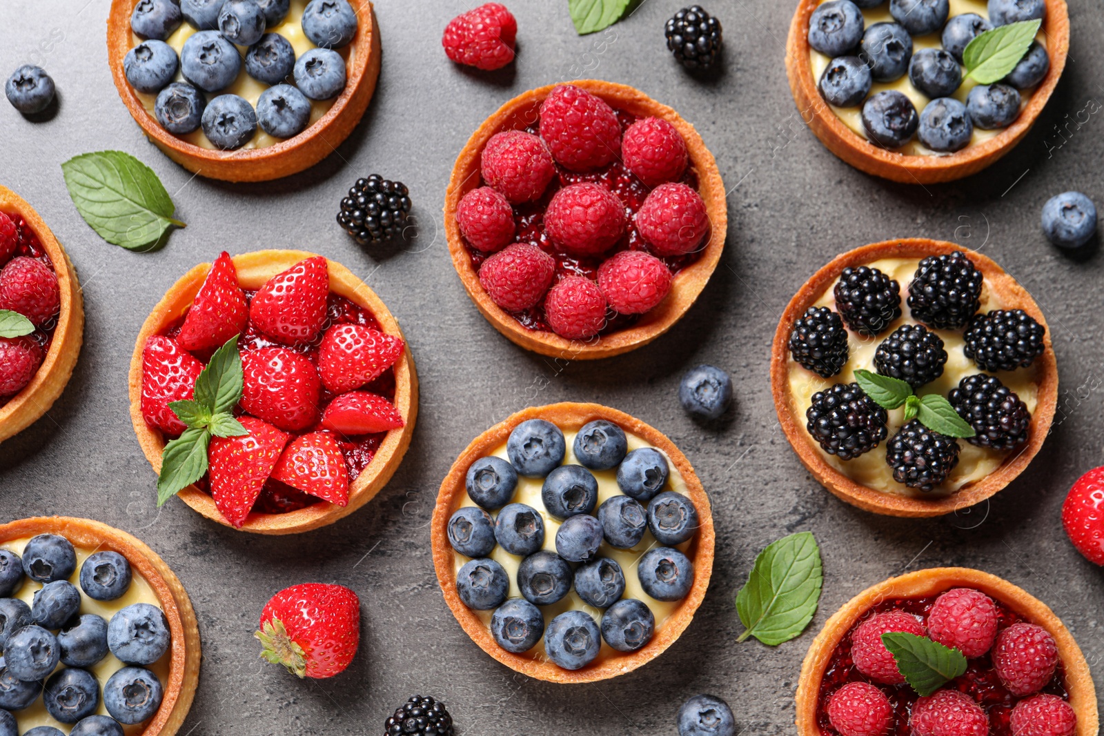 Photo of Tartlets with different fresh berries on grey table, flat lay. Delicious dessert