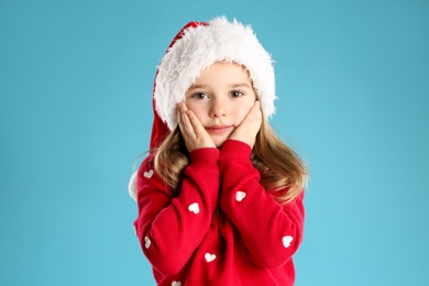 Photo of Cute child in Santa hat on light blue background. Christmas celebration