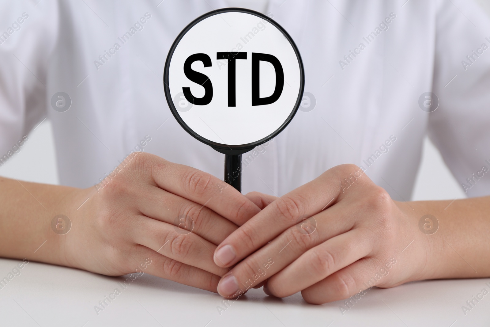 Photo of Doctor holding magnifying glass with abbreviation STD at white table, closeup