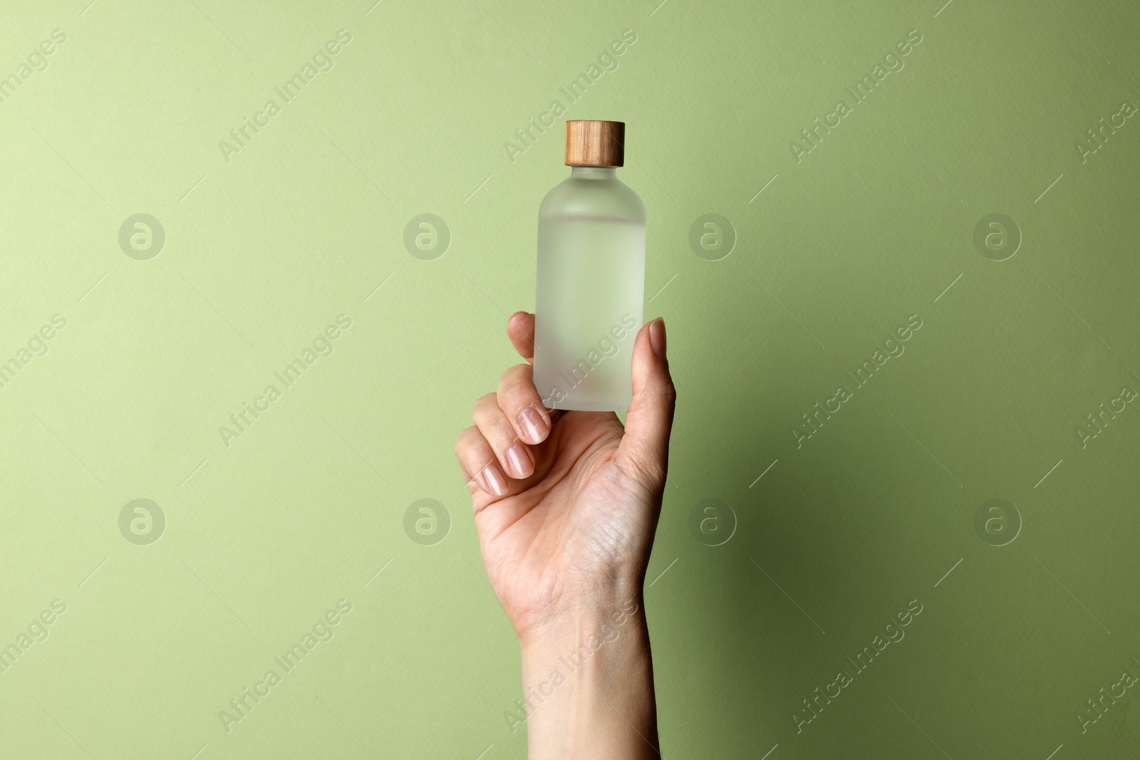 Photo of Woman holding bottle of cosmetic product on pale olive background, closeup. Space for text