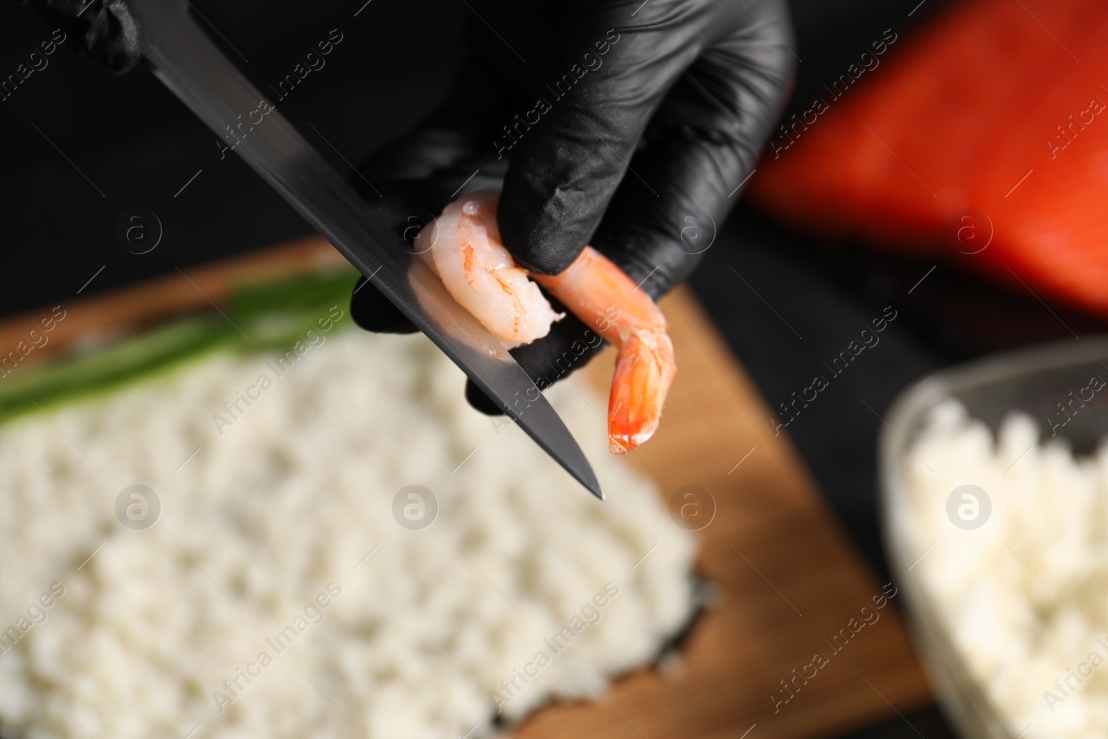 Photo of Chef in gloves peeling shrimp for sushi roll at table, closeup