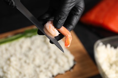 Photo of Chef in gloves peeling shrimp for sushi roll at table, closeup