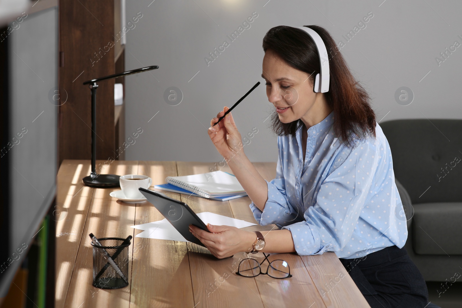 Photo of Woman with modern tablet and headphones learning at table indoors