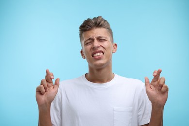 Photo of Emotional young man crossing his fingers on light blue background