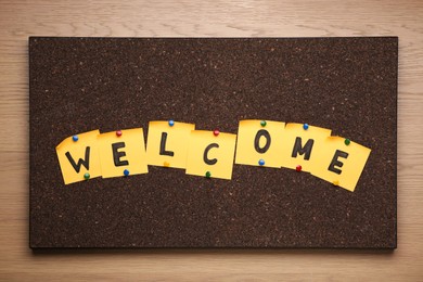 Photo of Corkboard with word Welcome made of paper notes on wooden background, top view