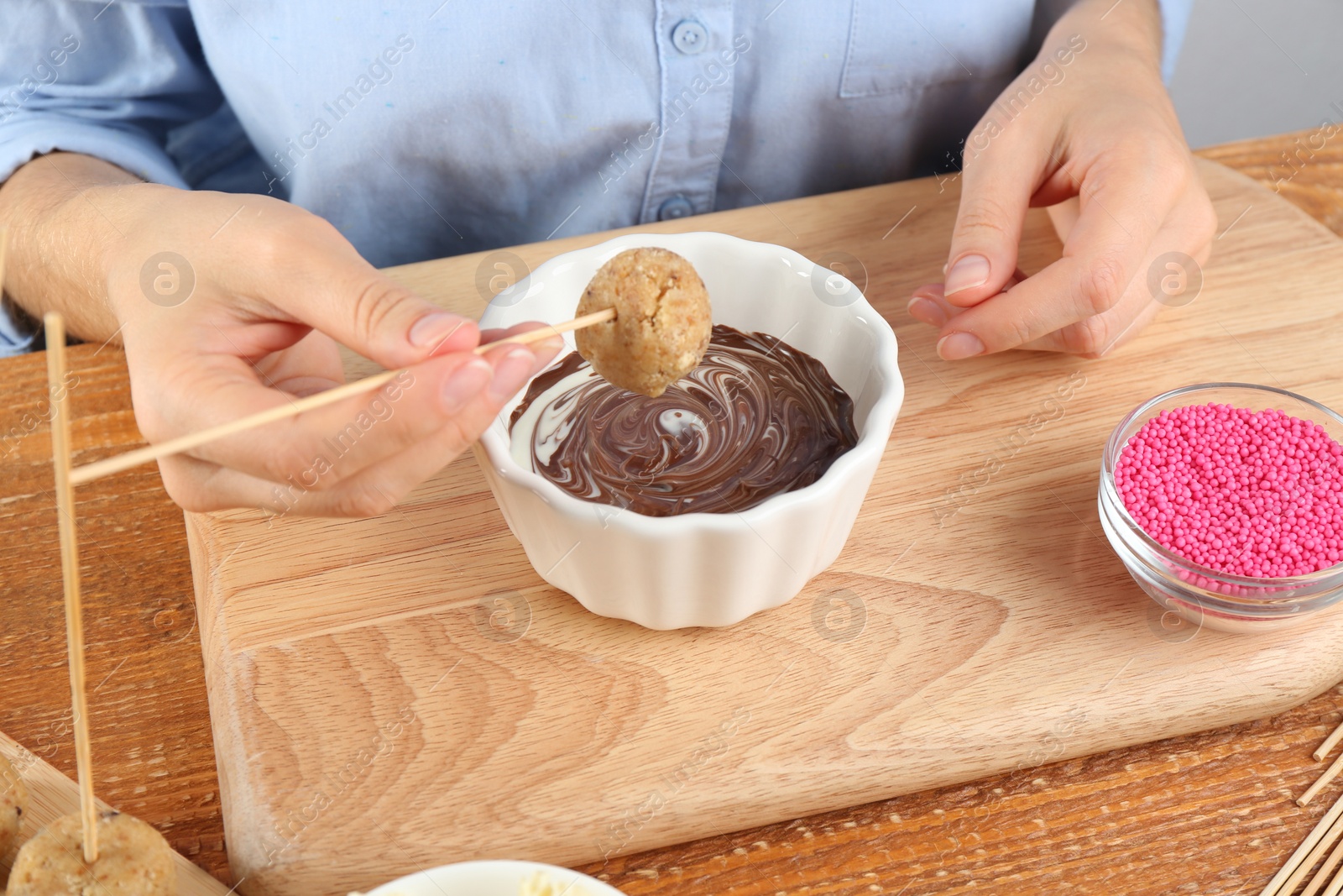 Photo of Young woman with cake pop and chocolate frosting at wooden table, closeup