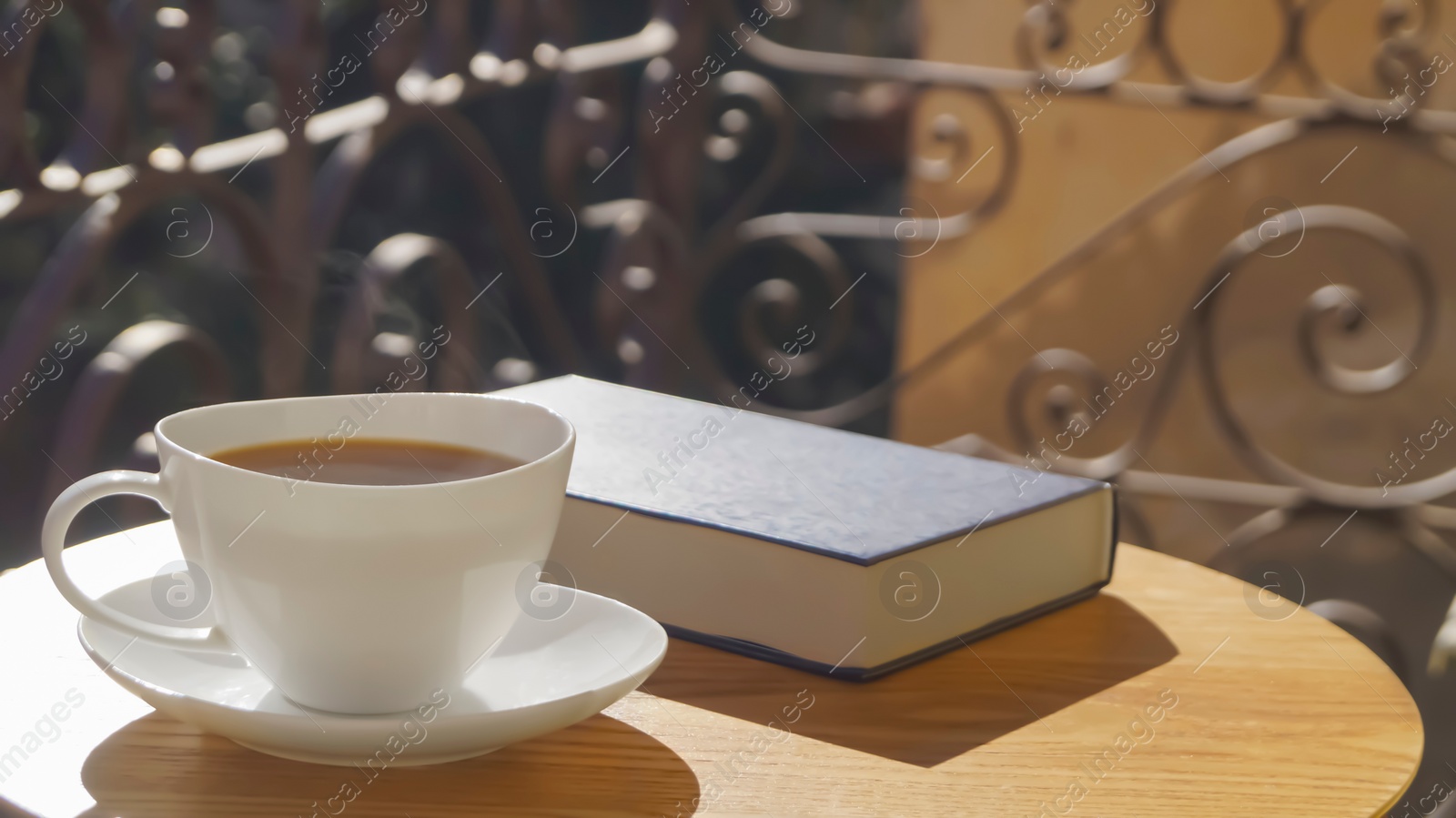 Photo of Cup of aromatic coffee and book on wooden table outdoors, space for text