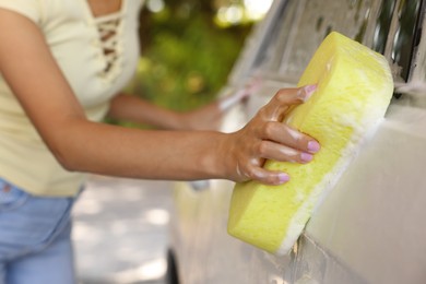 Photo of Woman washing car with sponge outdoors, closeup