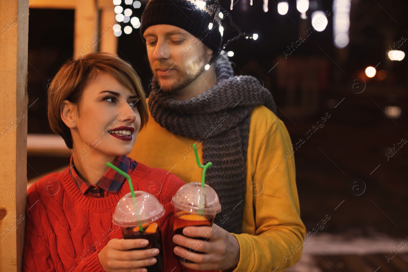 Photo of Young couple with cups of mulled wine at winter fair. Space for text