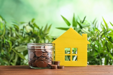 House model and jar with coins on wooden table against blurred background. Space for text