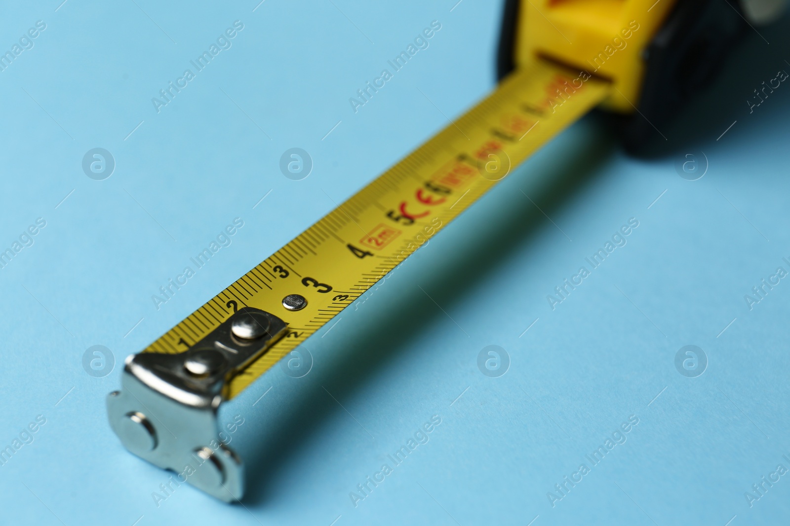 Photo of Tape measure on light blue background, closeup. Construction tool