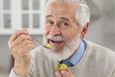 Happy senior man eating kiwi with spoon indoors