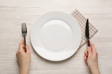 Photo of Woman with empty plate and cutlery at white wooden table, top view