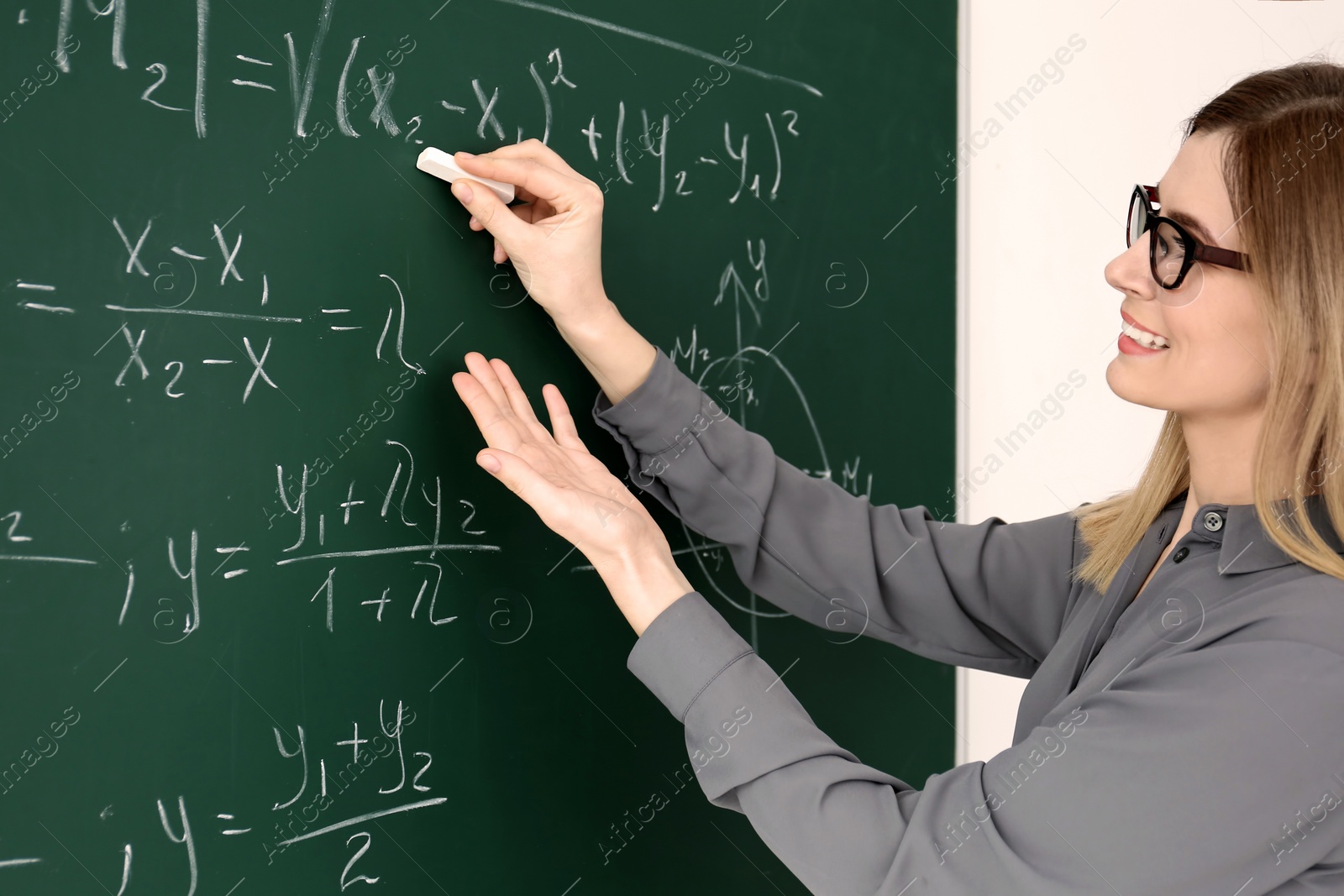 Photo of Young female teacher writing on blackboard in classroom