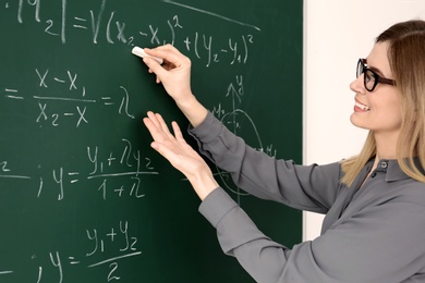 Young female teacher writing on blackboard in classroom