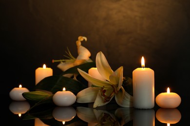 Photo of White lilies and burning candles on black mirror surface in darkness, space for text. Funeral symbols