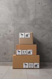 Photo of Many closed cardboard boxes with packaging symbols on floor near grey wall. Delivery service