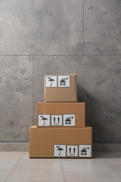 Many closed cardboard boxes with packaging symbols on floor near grey wall. Delivery service