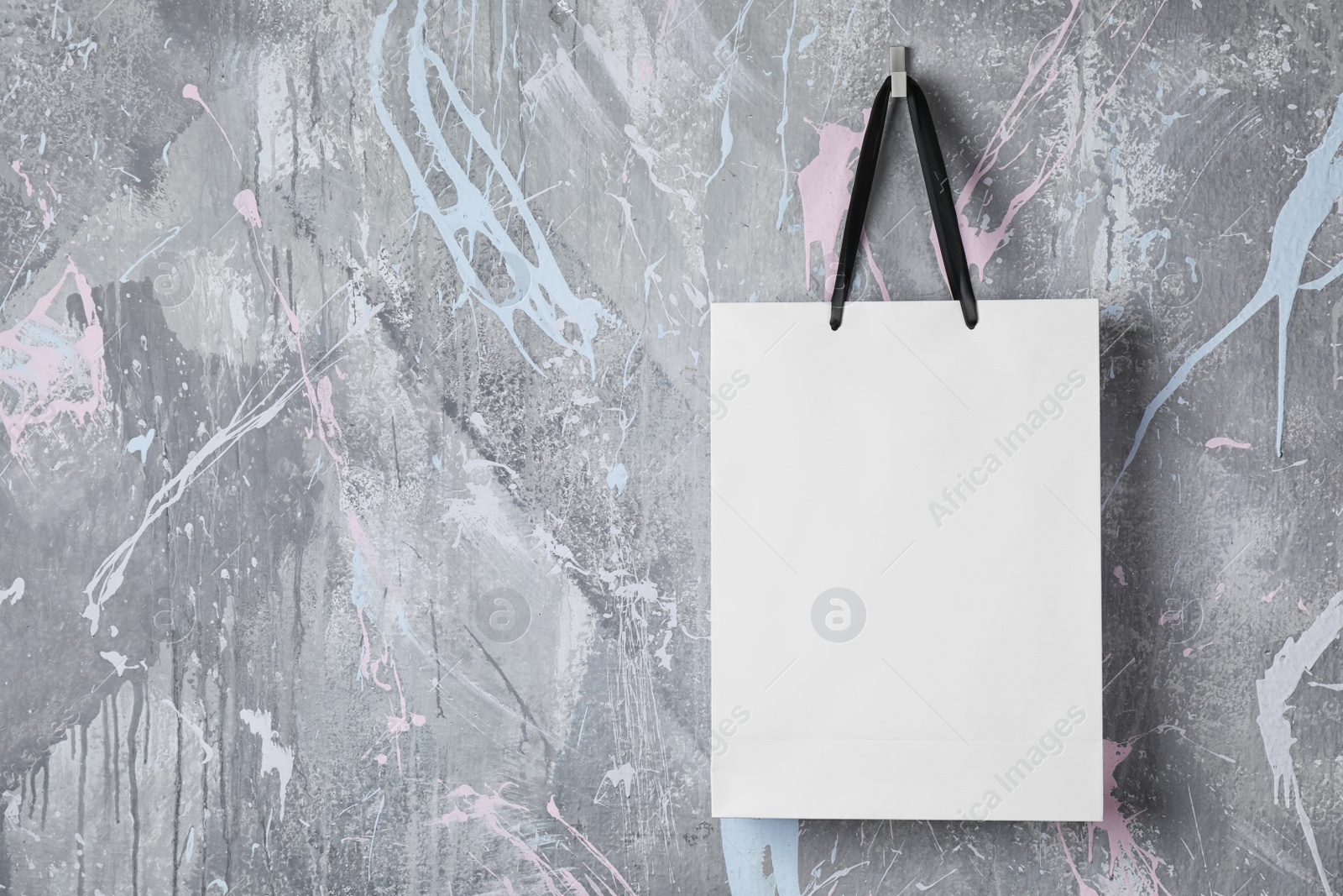 Photo of Paper shopping bag with handles hanging on color wall. Mock up for design