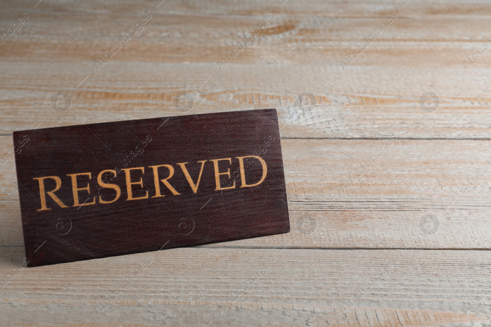 Photo of Elegant sign RESERVED on wooden surface, space for text. Table setting element