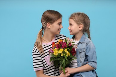 Photo of Little daughter congratulating her mom with flowers on light blue background. Happy Mother's Day