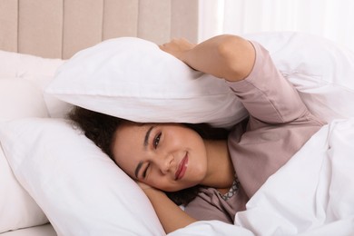 Photo of African American woman covering head with pillow in bed at home