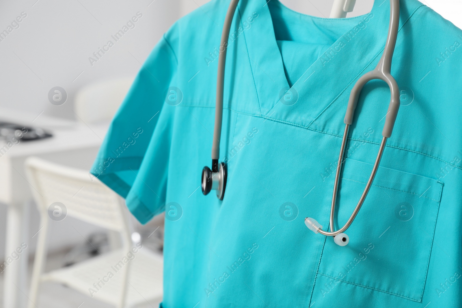 Photo of Turquoise medical uniform and stethoscope on rack in clinic, closeup