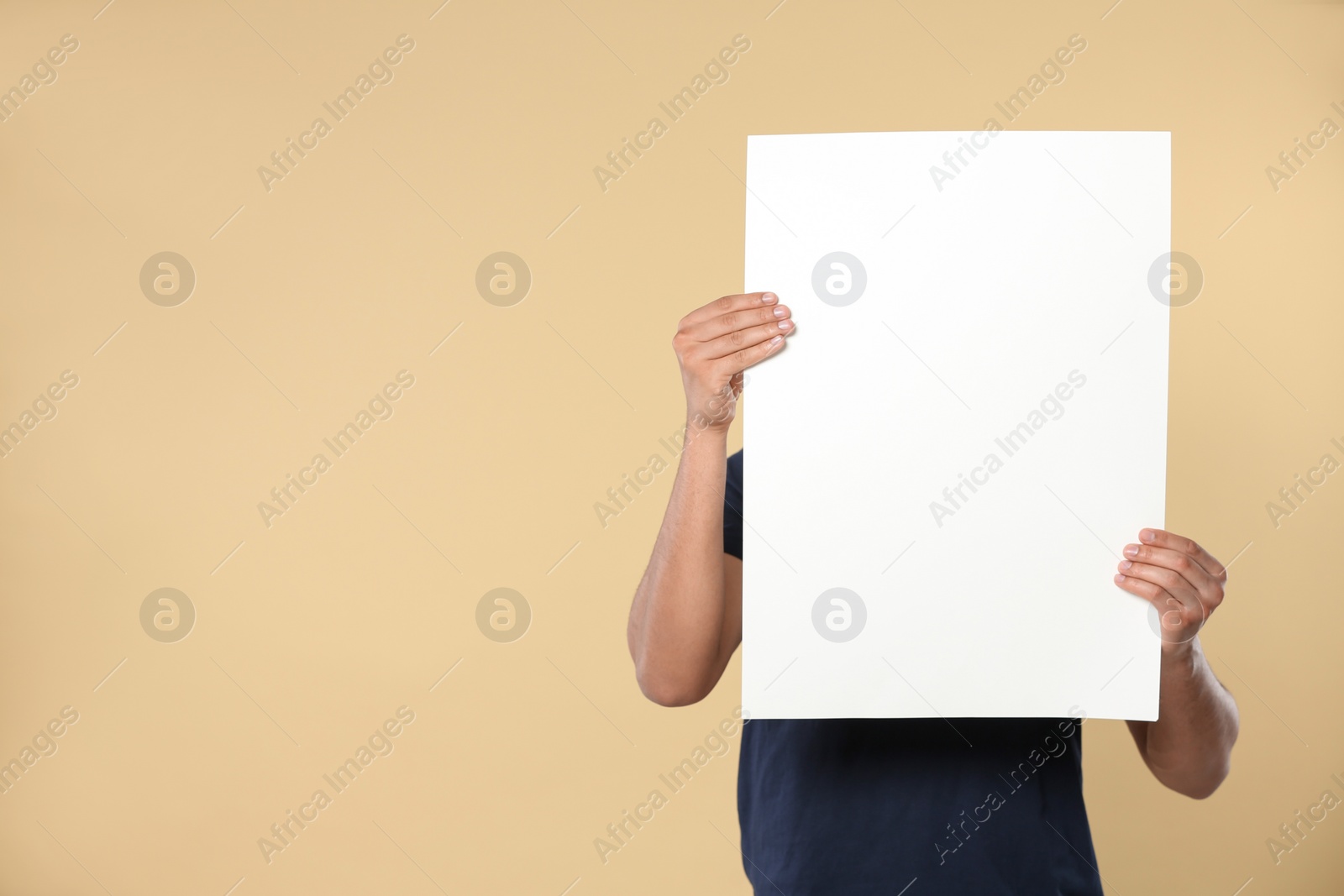 Photo of Man holding sheet of paper on beige background, closeup. Mockup for design