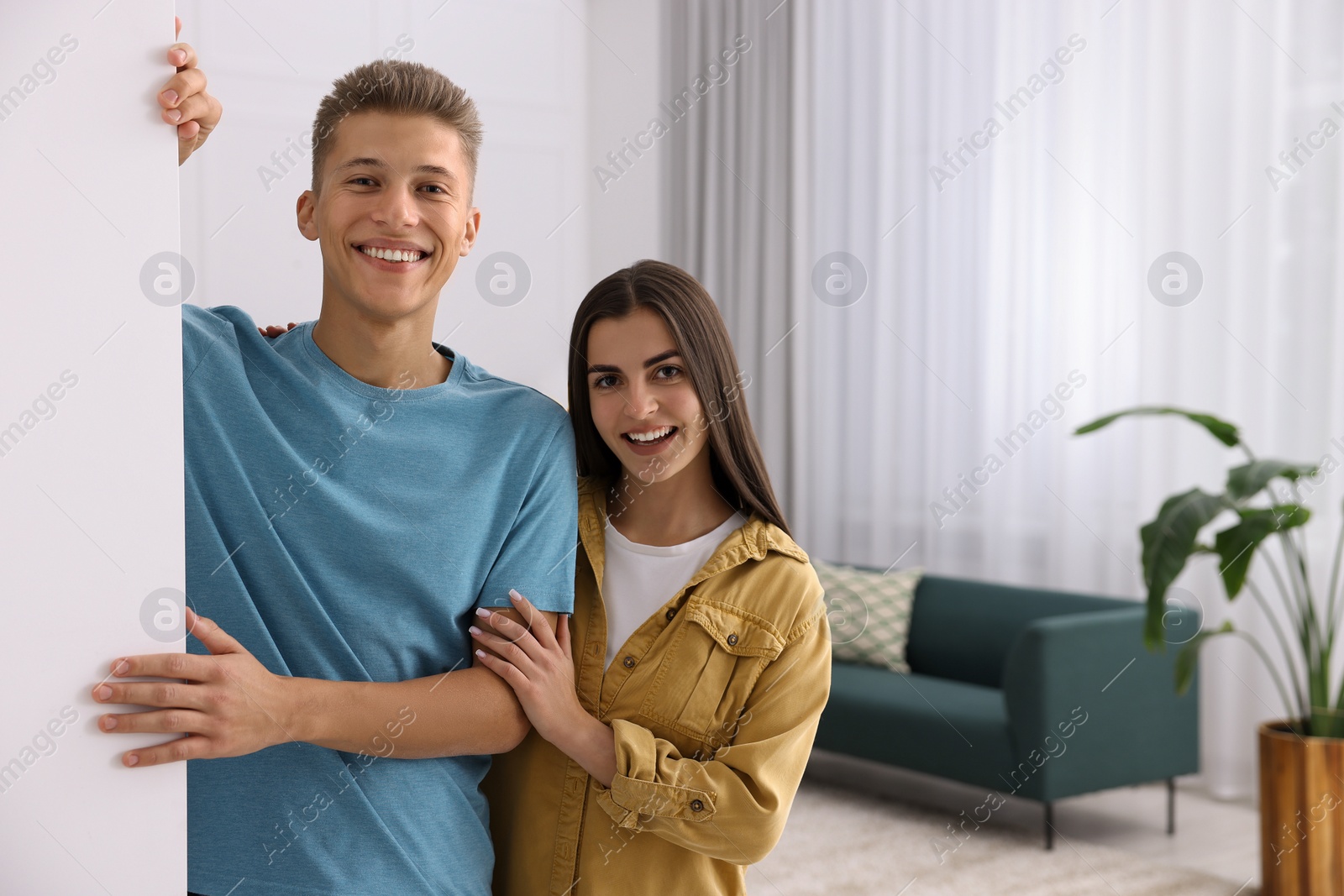 Photo of Happy couple standing near white wall at home, space for text. Invitation to come in room