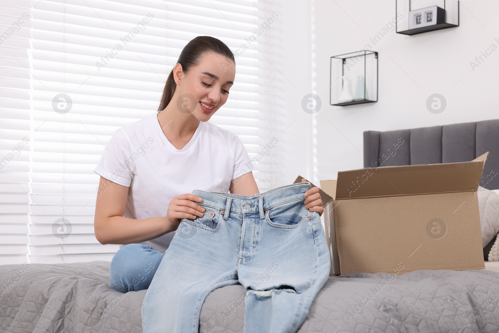 Photo of Happy woman with stylish light blue jeans at home. Online shopping