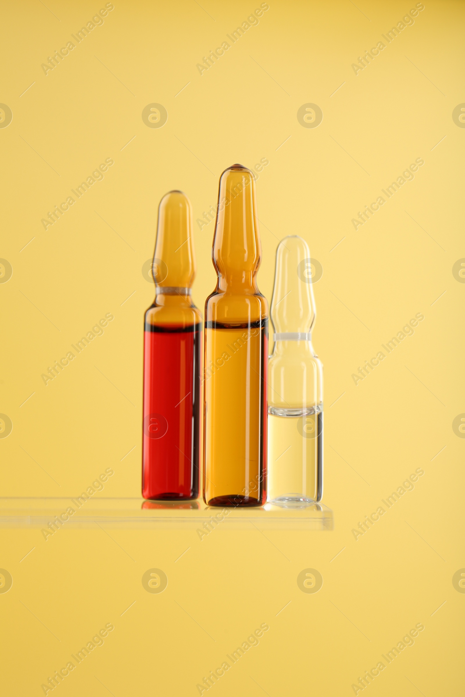 Photo of Glass ampoules with liquid on yellow background