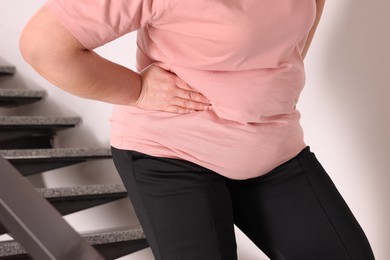 Overweight mature woman suffering from pain in right side on stairs indoors, closeup