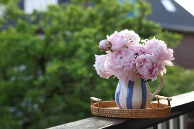 Beautiful pink peony flowers in vase on balcony railing outdoors. Space for text